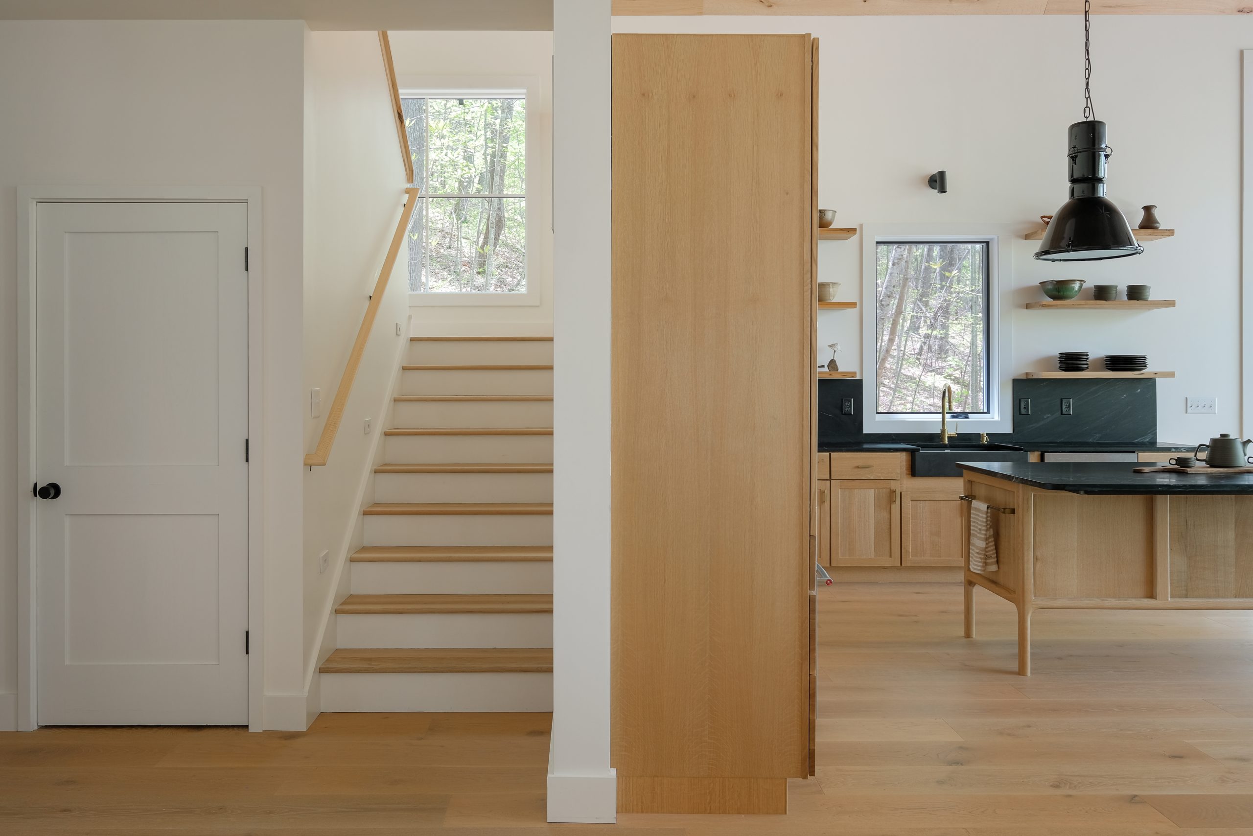 A clean, straight-run staircase in an Asheville custom home designed by Assembly Architecture + Build, featuring white risers and wood guardrails that create an open, modern look.