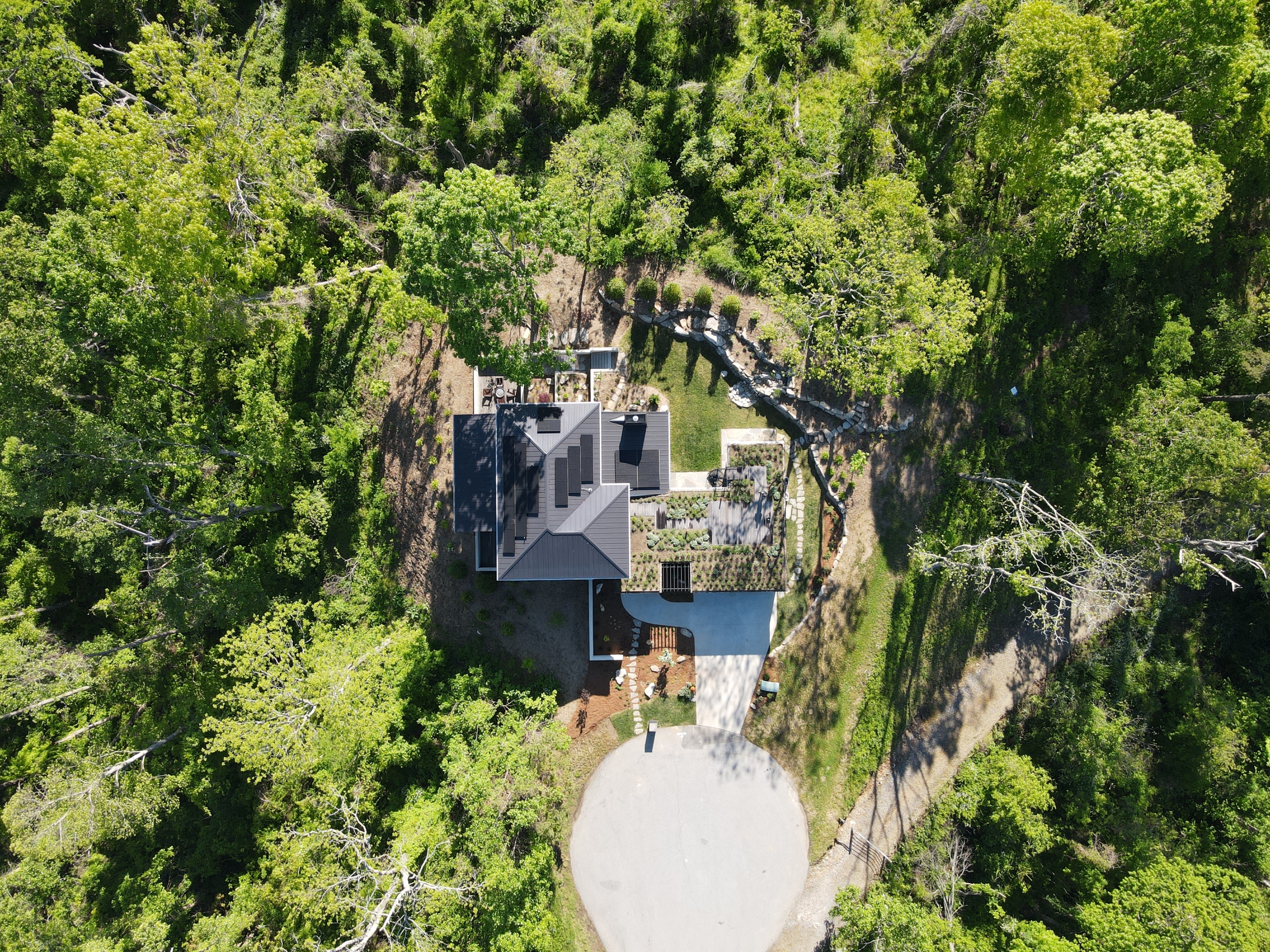 Drone shot of a net-positive home featuring solar panels and a green roof. the home is black and stands out in the nature it is surrounded by.