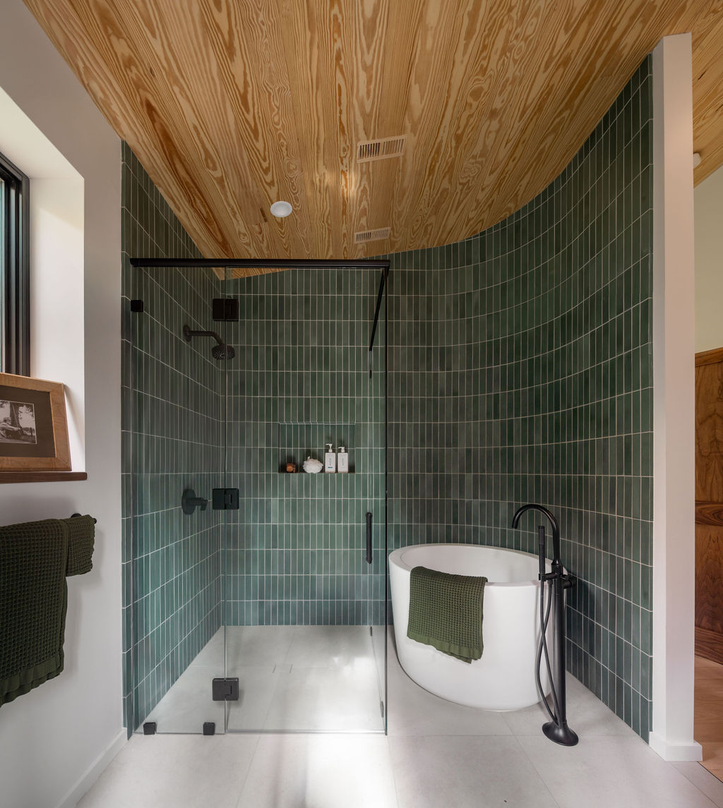 Luxury Asheville bathroom with emerald green tiles, freestanding tub, floor-to-ceiling windows, wood sloped ceiling & water-saving fixtures